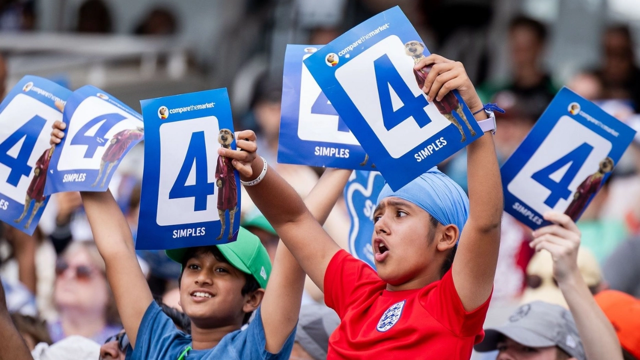 Young cricket fans cheer and hold up '4' signs during a match to celebrate a boundary at the stadium