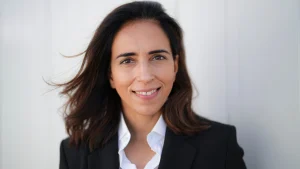 Portrait of Aarti Dabas in a black blazer and white shirt, smiling in front of a light background