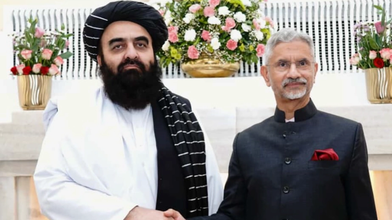 Afghanistan Foreign Minister Amir Khan Muttaqi and India’s External Affairs Minister S. Jaishankar shaking hands during a diplomatic meeting, with floral arrangements in the background.