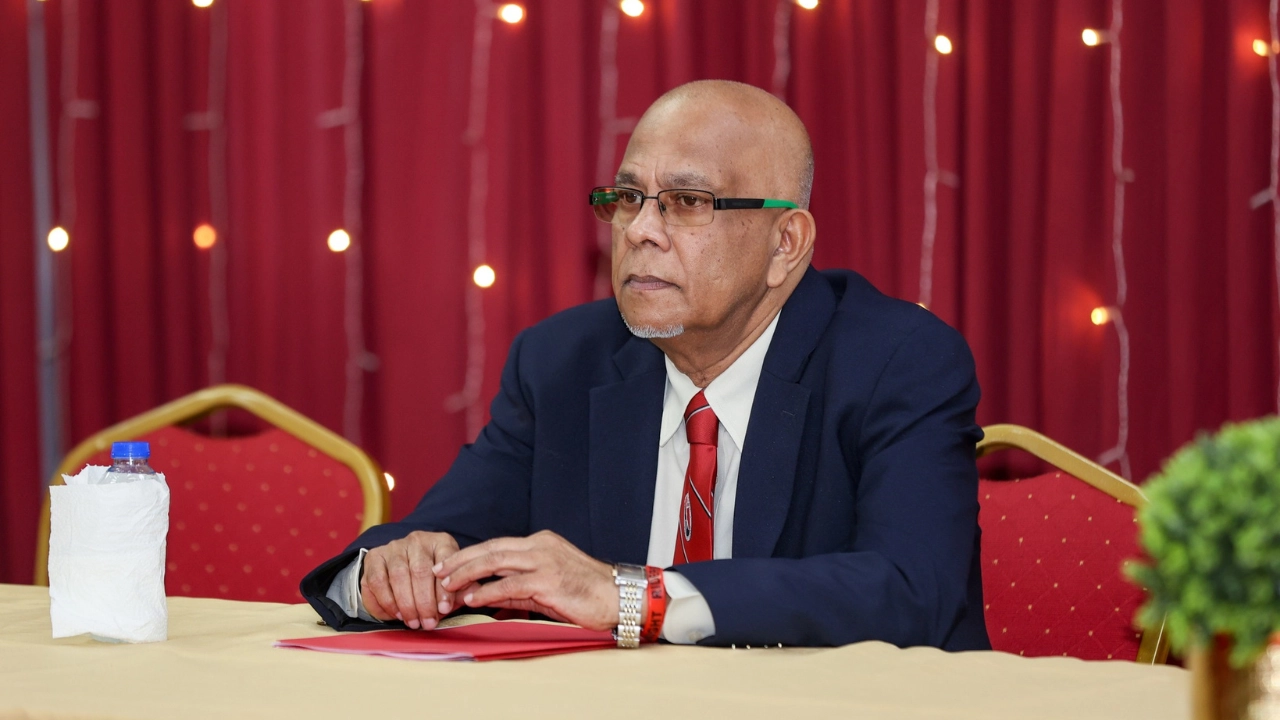 Azim Bassarath seated at a table during an official event, wearing a navy suit and red tie, representing Cricket West Indies leadership.