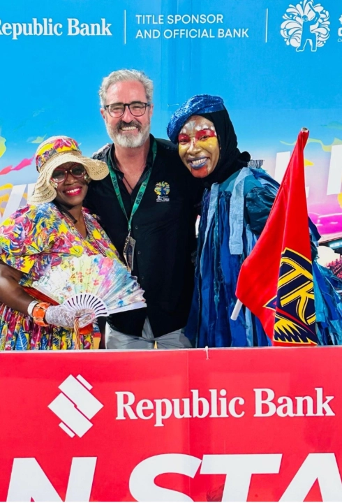 CPL Commercial Director Jamie Stewart posing with colorful Caribbean Premier League fans, featuring festive costumes and Republic Bank branding in the background.