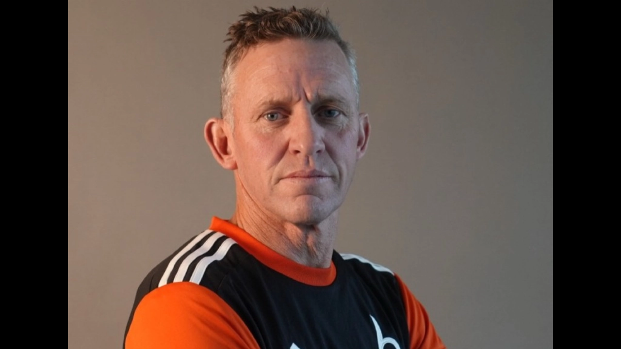 Portrait of Craig Cumming wearing a black and orange sports shirt, looking serious against a plain background
