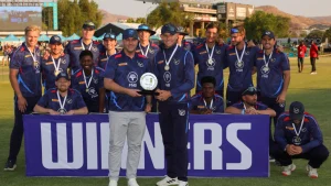 Cricket Namibia men's team celebrating with the trophy after winning a T20 series, posing with medals and a winners banner on the field.