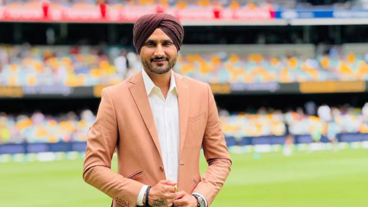 Harbhajan Singh standing at a cricket stadium wearing a brown blazer and turban