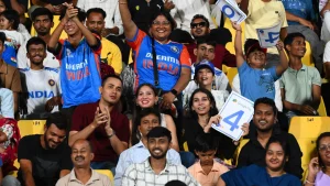 Indian cricket fans cheering and holding scorecards during a live match at the stadium