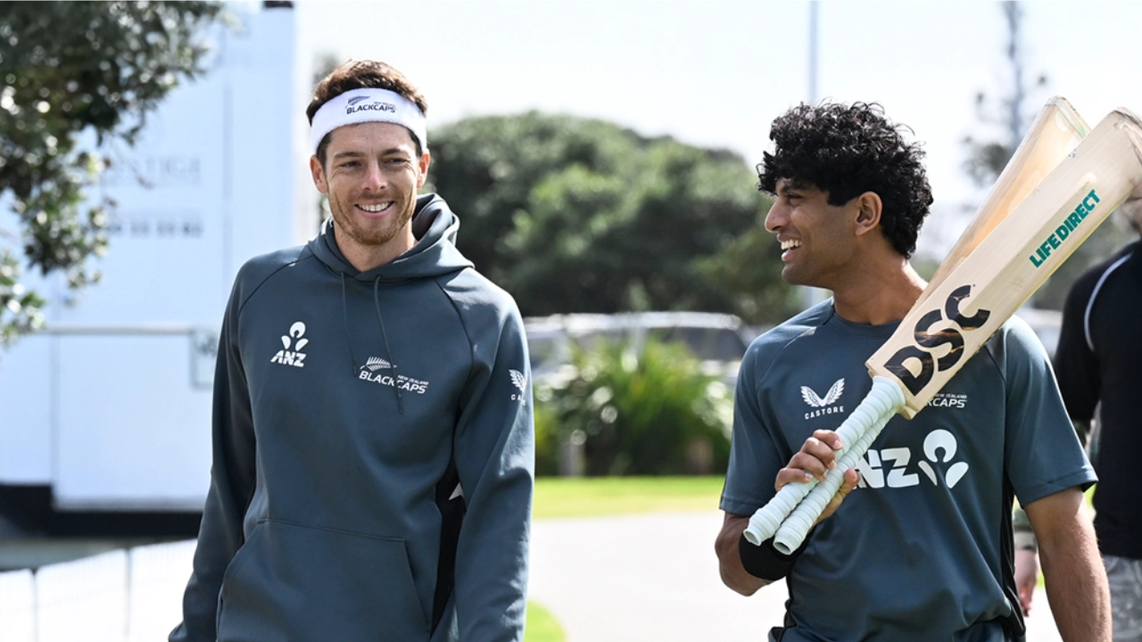 New Zealand cricketers Mitchell Santner and Rachin Ravindra walking and smiling during training, with Ravindra carrying two DSC cricket bats.