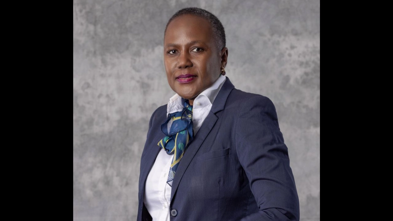 Professional portrait of Pearl Maphoshe in a navy suit and scarf against a gray textured background.