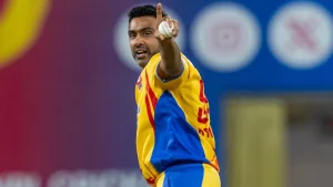 Ravichandran Ashwin celebrates after taking a wicket, pointing upward while wearing a yellow and blue cricket jersey