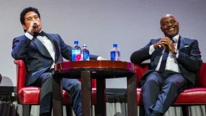 Sachin Tendulkar and Brian Lara seated on stage in formal attire speaking at a cricket legends event
