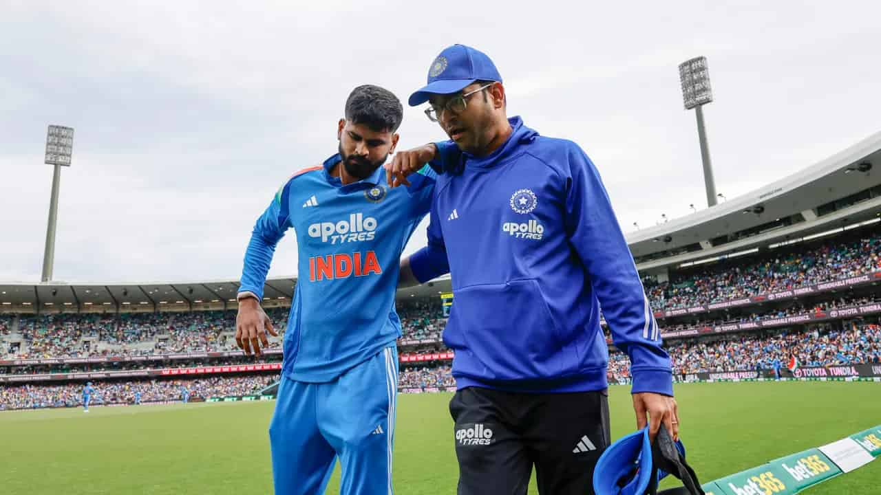 Indian cricketer Shreyas Iyer walks off the field with team staff support during a match, wearing the blue India jersey.
