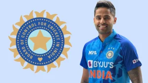 Surya Kumar Yadav in Indian cricket team jersey standing next to the BCCI logo on a light blue background