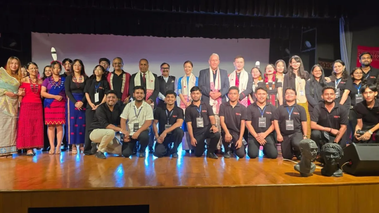 Group photo of TEDx event speakers, volunteers, and participants in cultural attire on stage after the event