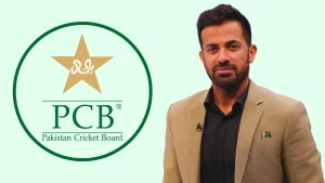 Wahab Riaz standing beside the Pakistan Cricket Board (PCB) logo wearing a beige blazer with a Pakistan flag pin