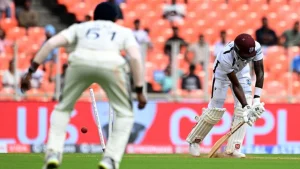 West Indies Test cricketer getting bowled during a match, with Indian fielder in foreground