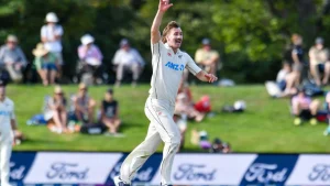 Blair Tickner of New Zealand celebrates after taking a wicket during a Test match, wearing the official NZ Test jersey with spectators in the background