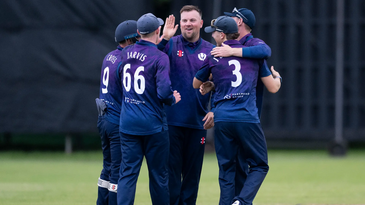 Cricket Scotland men's team players celebrate a wicket during a match in purple and navy team kit