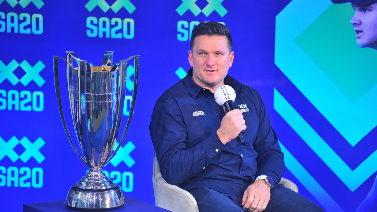 Graeme Smith speaking at a press event with the SA20 2025 trophy displayed beside him against a blue SA20-branded backdrop.