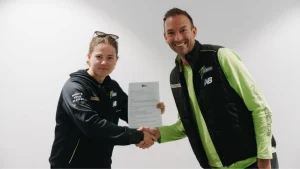 Hannah Darlington shakes hands with Trent Copeland while holding a signed contract, both wearing Sydney Thunder apparel.