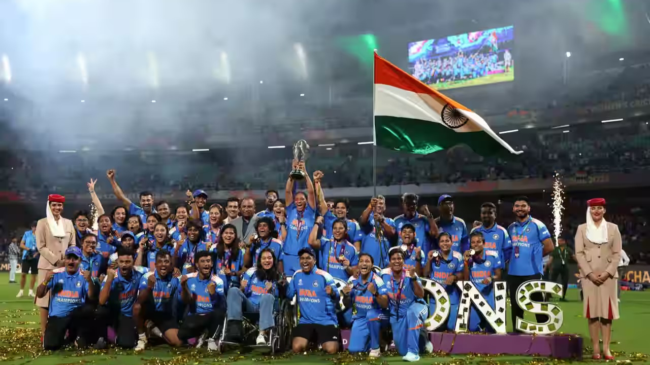 Indian Women's Cricket Team and support staff celebrating with the trophy and national flag after a championship win