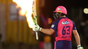 Jos Buttler raises his bat in celebration wearing the Rajasthan Royals jersey during an IPL match.