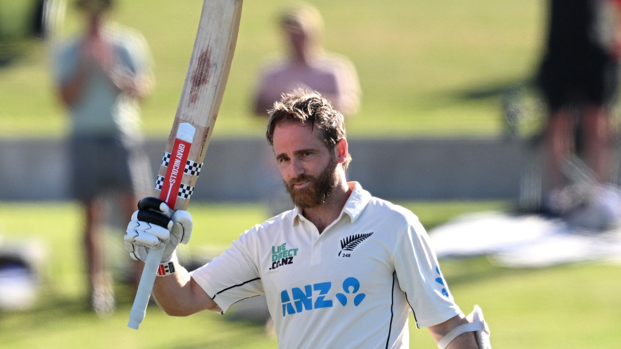 Kane Williamson raises his bat in celebration while wearing the New Zealand Test cricket jersey after reaching a milestone innings