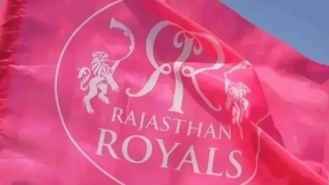 Close-up of the Rajasthan Royals team flag waving in the wind, featuring the team’s logo and vibrant pink color against a clear blue sky.