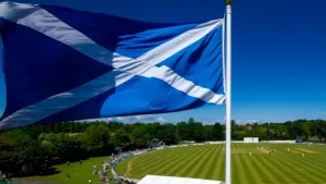 Scottish flag waving above a cricket ground during a match on a sunny day