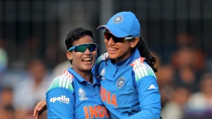 Smriti Mandhana and Deepti Sharma celebrate during a match for India at the ICC Women’s Cricket World Cup 2025, both wearing blue India jerseys and sunglasses.