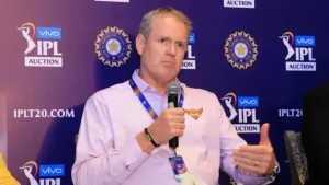 Tom Moody speaks into a microphone during an IPL auction event, wearing a Sunrisers Hyderabad shirt with IPL and BCCI branding in the background.