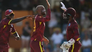 West Indies cricketers celebrate a wicket during a T20I match, with players in maroon kits exchanging high-fives on the field.
