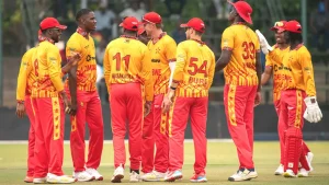 Zimbabwe national cricket team players huddle and celebrate during a match, wearing yellow and red team jerseys.