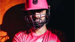 Babar Azam wearing a Sydney Sixers jersey and pink helmet in a dramatic portrait with shadow contrast