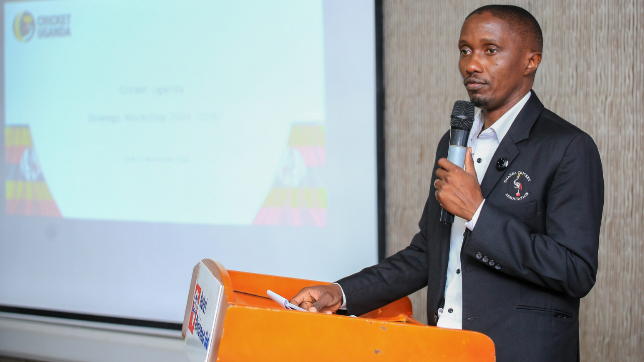 Cricket Uganda Chairman Jackson Kavuma speaking at the podium during the 2024–2027 strategy workshop, with a presentation slide in the background.