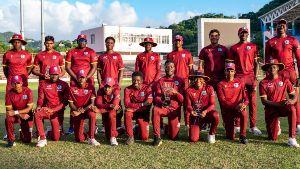 Group photo of the West Indies Under-19 cricket squad in maroon uniforms posing with trophies on the field