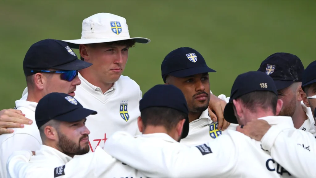 Durham County Cricket team players in a pre-match huddle wearing white kits and team caps