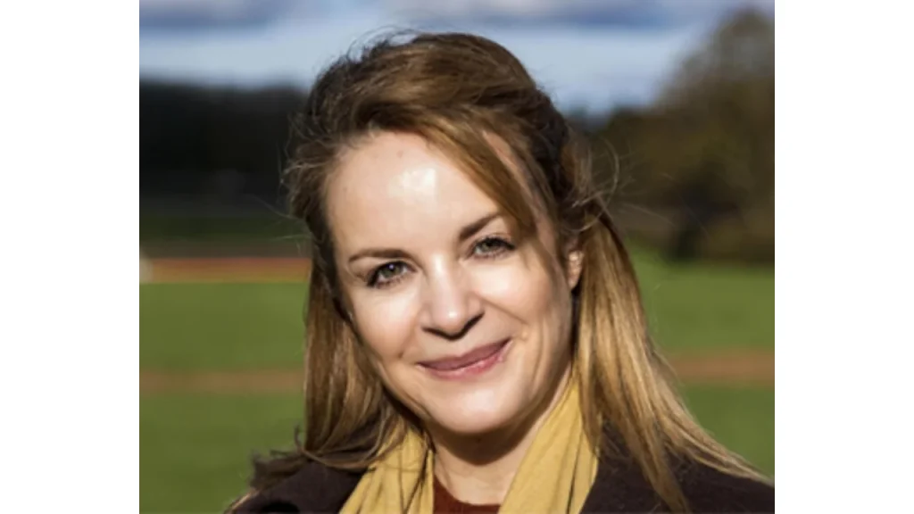 Portrait of Emma White, cricket administrator, smiling outdoors with a grassy field in the background.