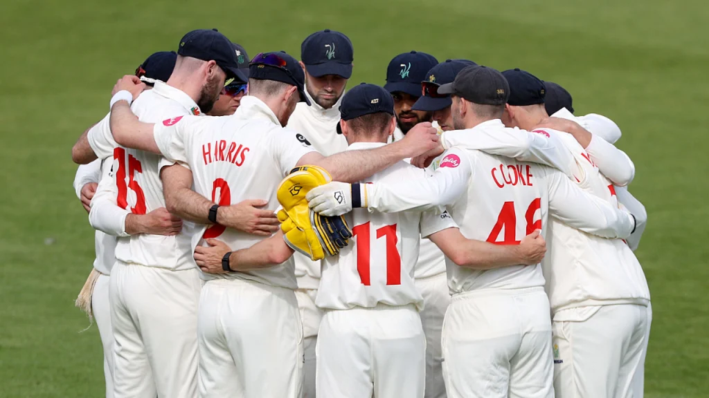 Glamorgan County Cricket Club players in a team huddle before a County Championship match, wearing white kits and navy caps