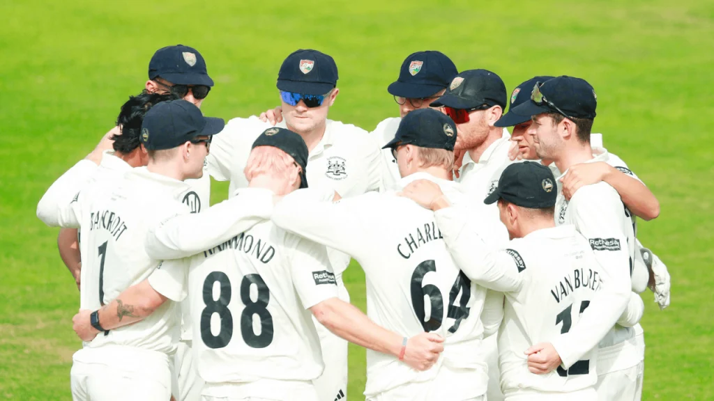 Gloucestershire County Cricket team players in a huddle on the field wearing white kits and caps before a match
