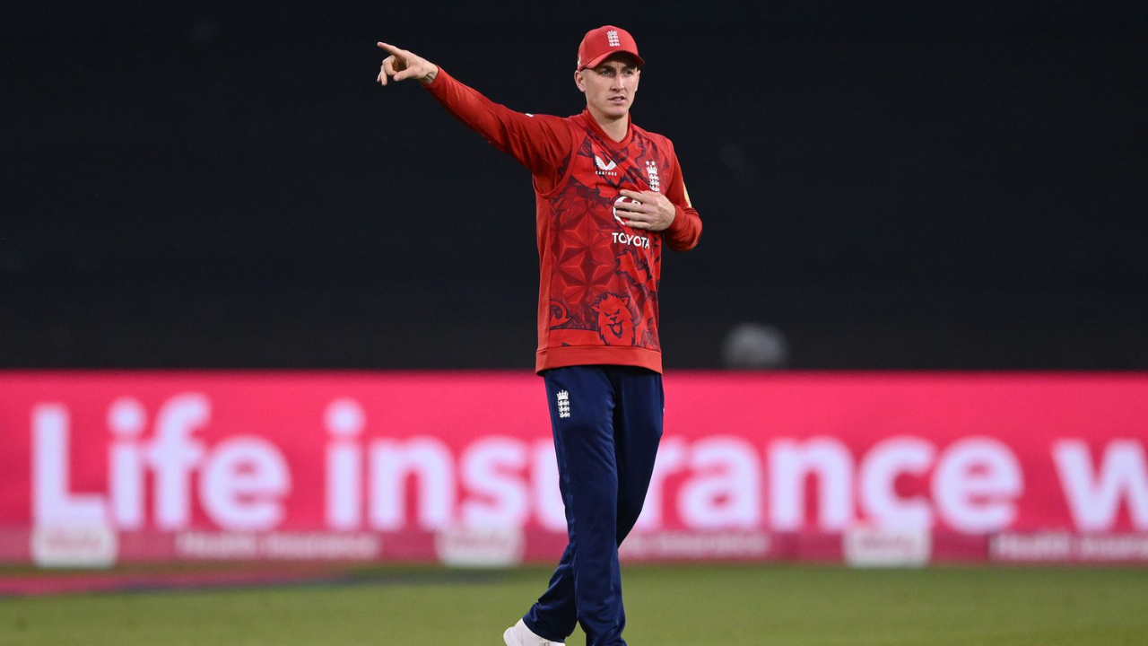 Harry Brook in England's T20 cricket kit pointing during a fielding session under stadium lights.