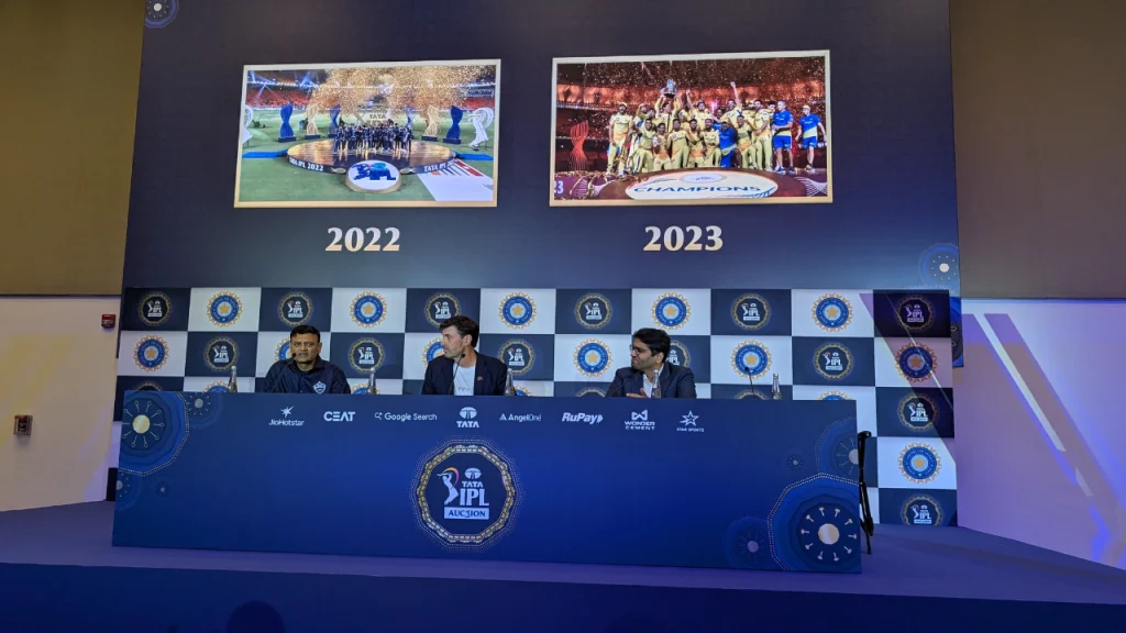 Hemang Badani, Stephen Fleming, and Shashwat Goenka seated at the IPL Auction 2024 panel with 2022 and 2023 champion images in the background