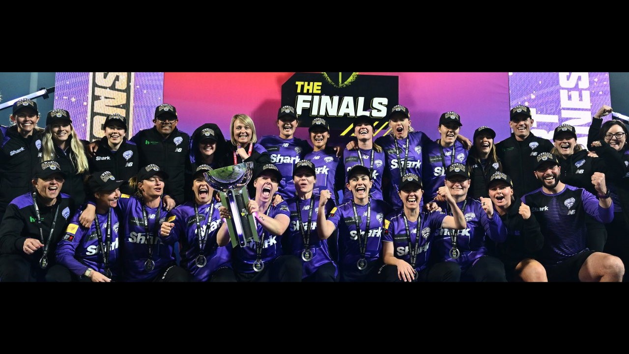 Hobart Hurricanes women's cricket team celebrating WBBL11 championship victory with trophy and medals on stage.