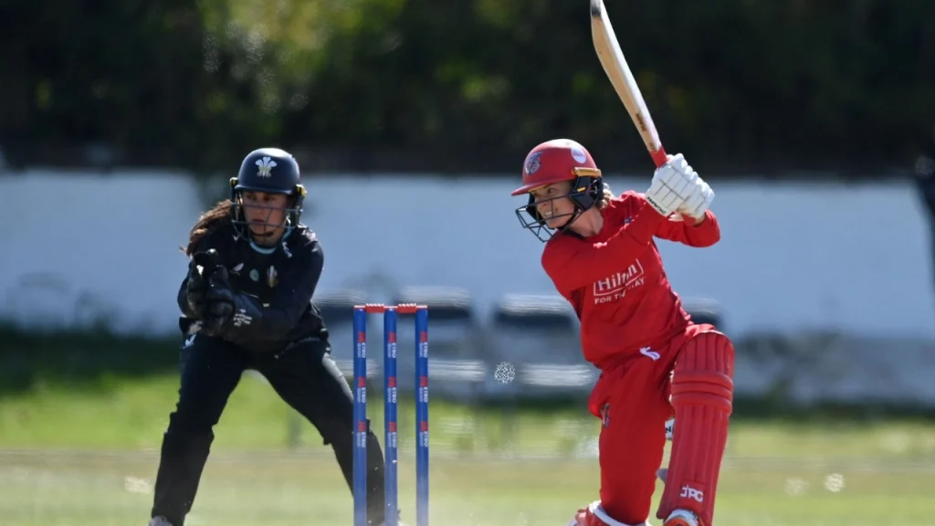 Katie Mack plays a cover drive while batting against Surrey in a women's domestic cricket match, with wicketkeeper ready behind the stumps