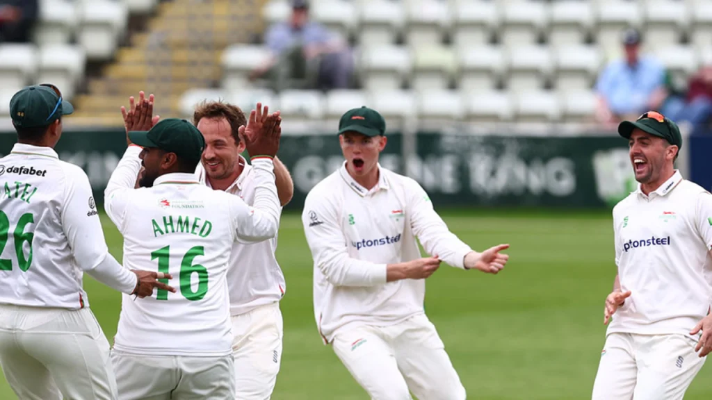 Leicestershire players celebrating a wicket during a County Championship match, wearing white kits on the field