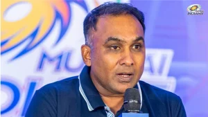 Mahela Jayawardene speaking into a microphone during a Mumbai Indians press conference with team logo in the background