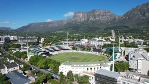 Aerial view of Newlands Cricket Ground in Cape Town with surrounding buildings and mountainous backdrop on a clear day.