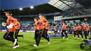 Perth Scorchers WBBL team running onto the field at Blundstone Arena in Hobart ahead of a match, wearing orange and black kits