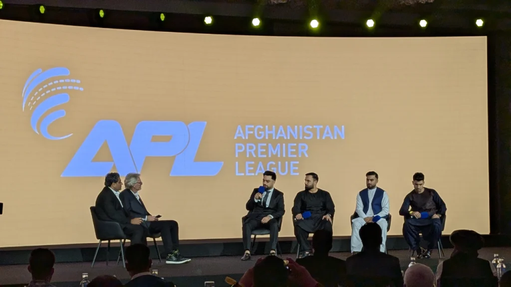 Rashid Khan, Mohammad Nabi, Hashmatullah Shahidi, and Rahmanullah Gurbaz speaking on the players’ panel during the Afghanistan Premier League 2025 event, with APL branding in the background.
