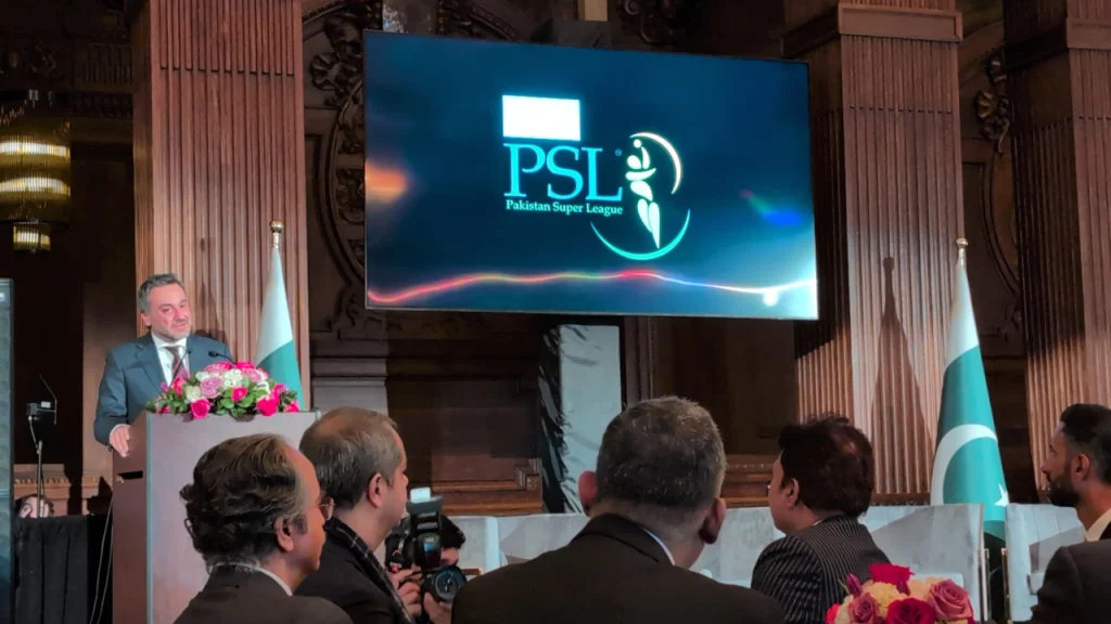 Salman Naseer delivering a speech at the Pakistan Super League (PSL) Roadshow in New York, with PSL logo on screen and Pakistan flags in the background