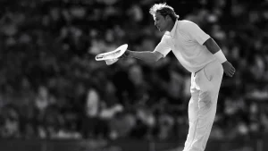 Shane Warne acknowledges the crowd during a cricket match, captured in a black and white tribute photograph.