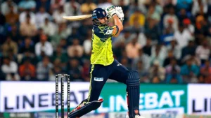 Tim David playing a powerful shot during a T10 League 2025 cricket match in front of a packed stadium.